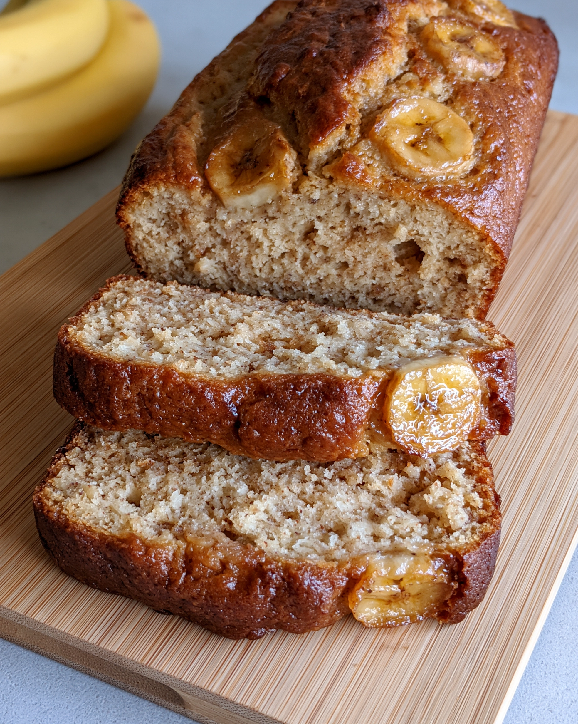 Easy banana bread recipe sliced on a wooden board with banana slices on top