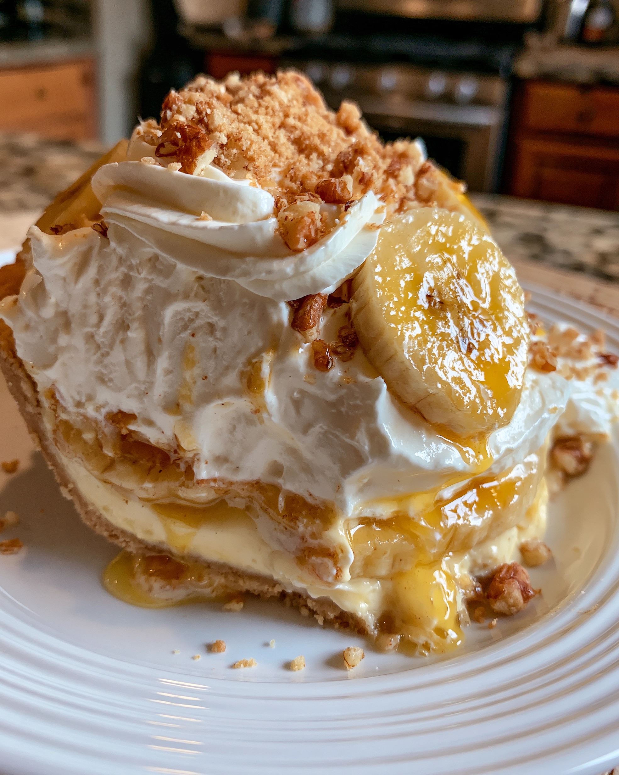 Easy banana cream pie recipe — a tall slice with silky vanilla custard, layers of fresh banana and clouds of whipped cream in a golden graham crust, topped with banana slices and toasted pecans