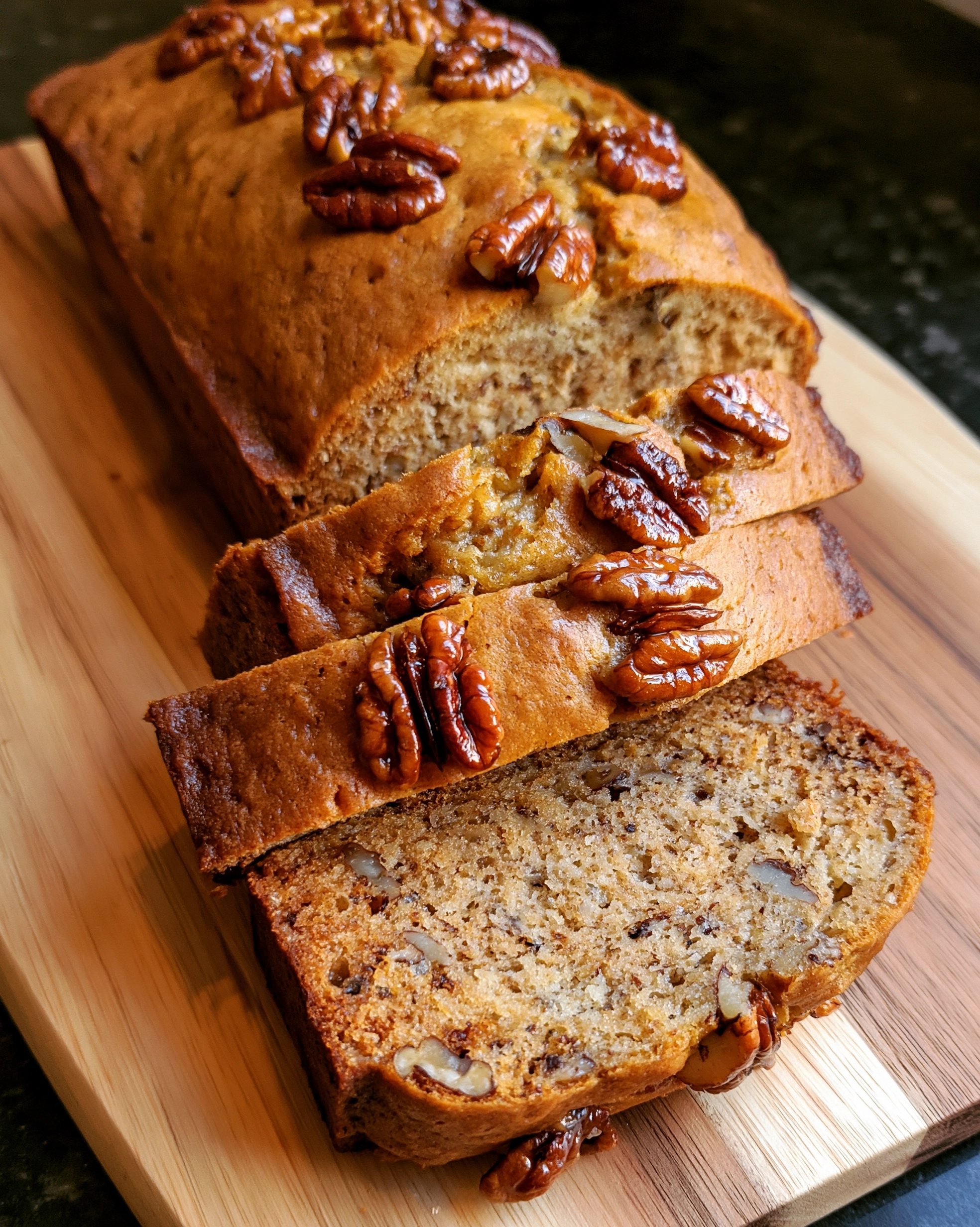 Easy banana nut bread recipe — golden loaf sliced on a wooden board, with chopped pecans in the moist, tender crumb and glossy pecan halves scattered over the top