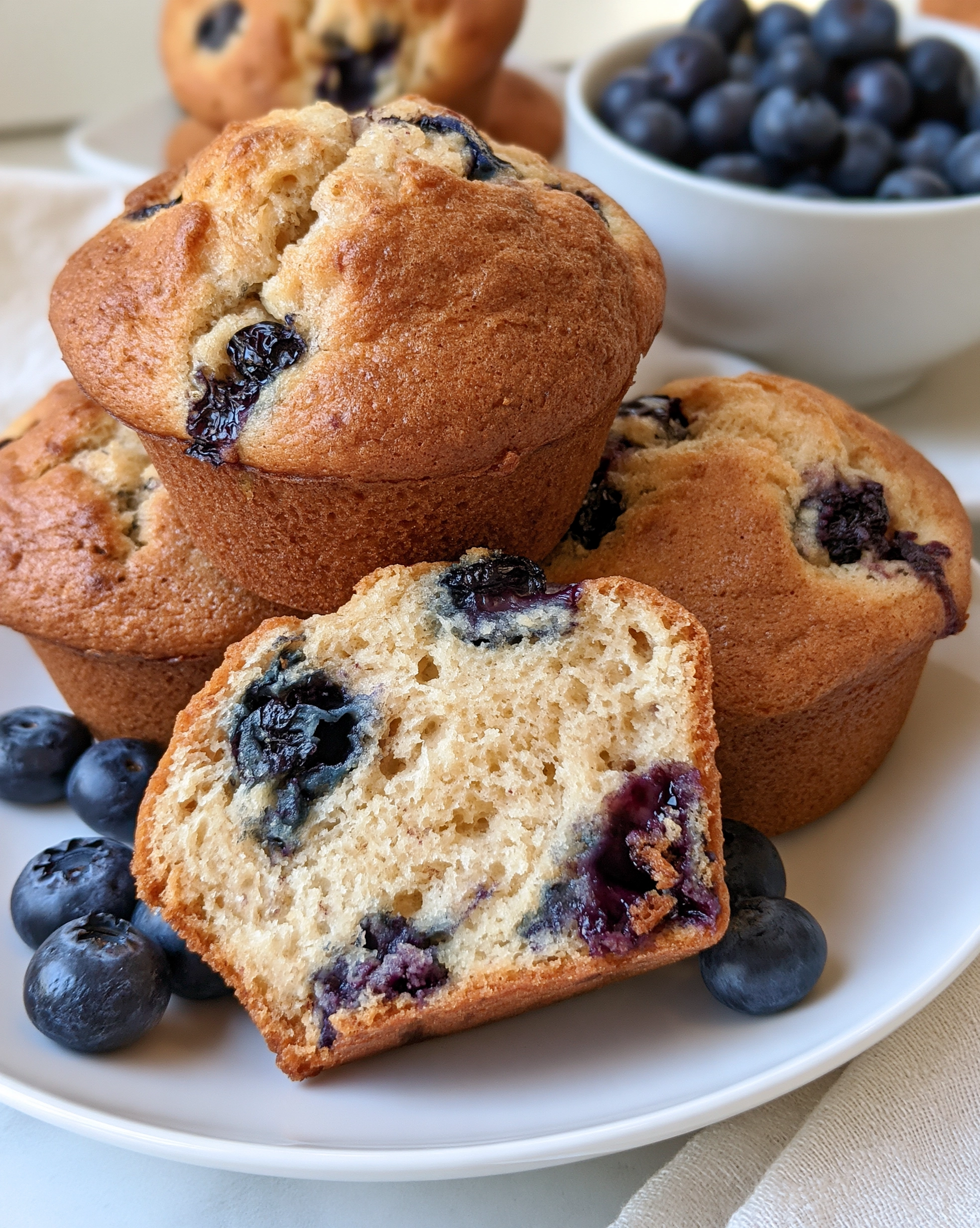 Easy blueberry muffins with tall golden domes and juicy blueberries, one muffin cut open to show the soft crumb