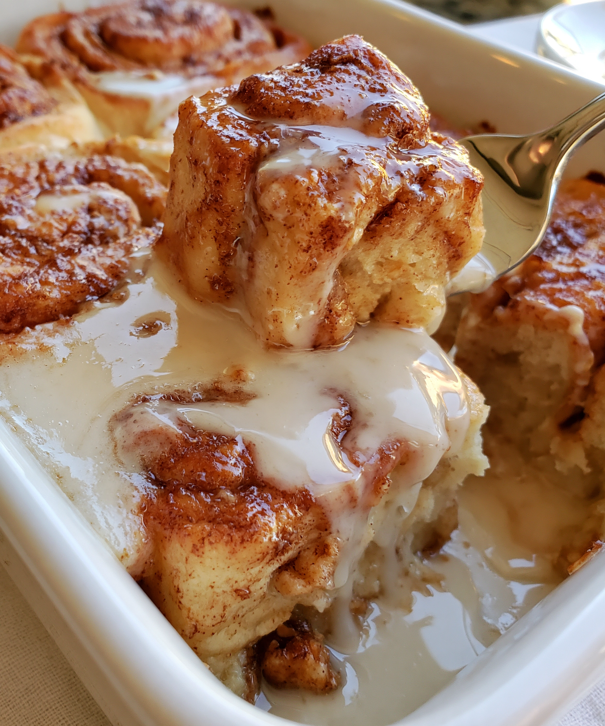 Easy cinnamon roll casserole recipe with golden cinnamon-swirled pieces and warm white icing dripping and pooling over the top in a white baking dish