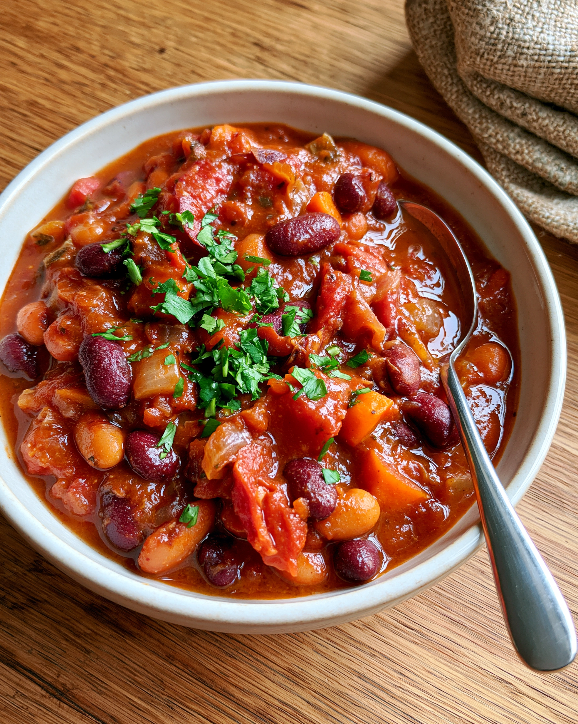 Easy vegetarian chili in a white bowl with kidney beans, white beans, sweet potato and tomatoes in a thick sauce, topped with fresh parsley