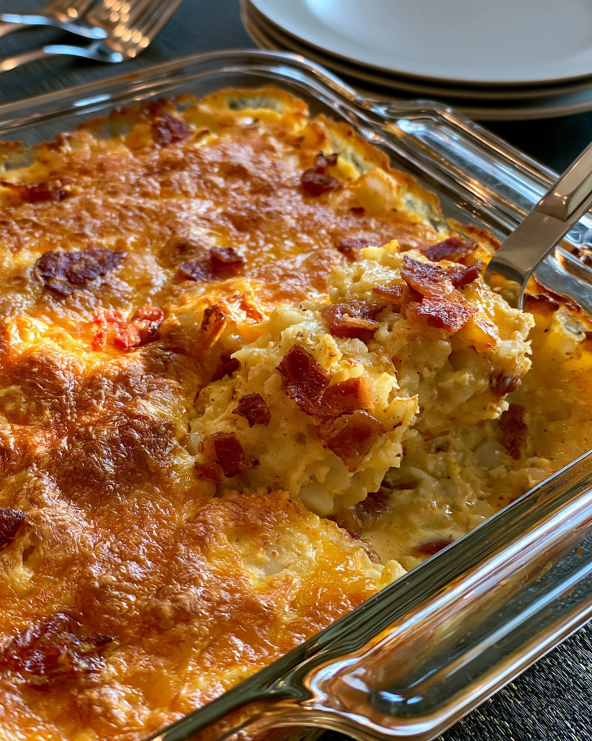 Easy hash brown casserole recipe in a glass baking dish with creamy shredded potatoes, a golden melted cheese top and crispy bacon pieces scattered over it