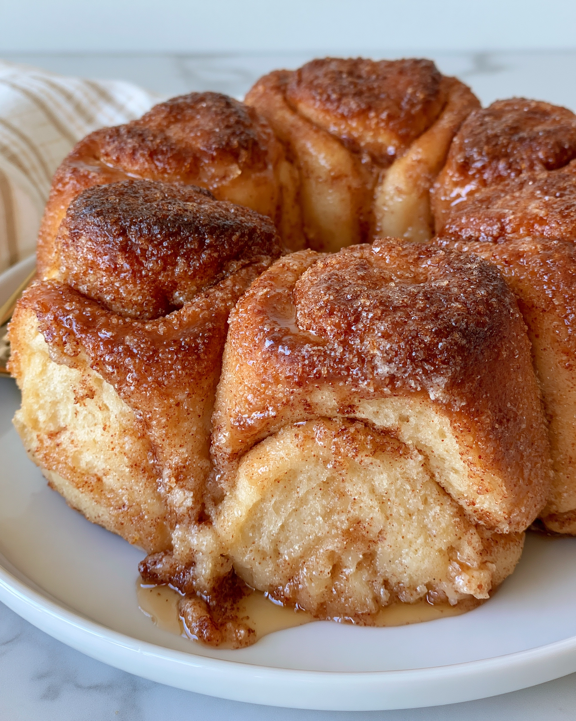 Easy monkey bread recipe — golden pull-apart bundt bread with a glossy cinnamon caramel glaze on a white plate