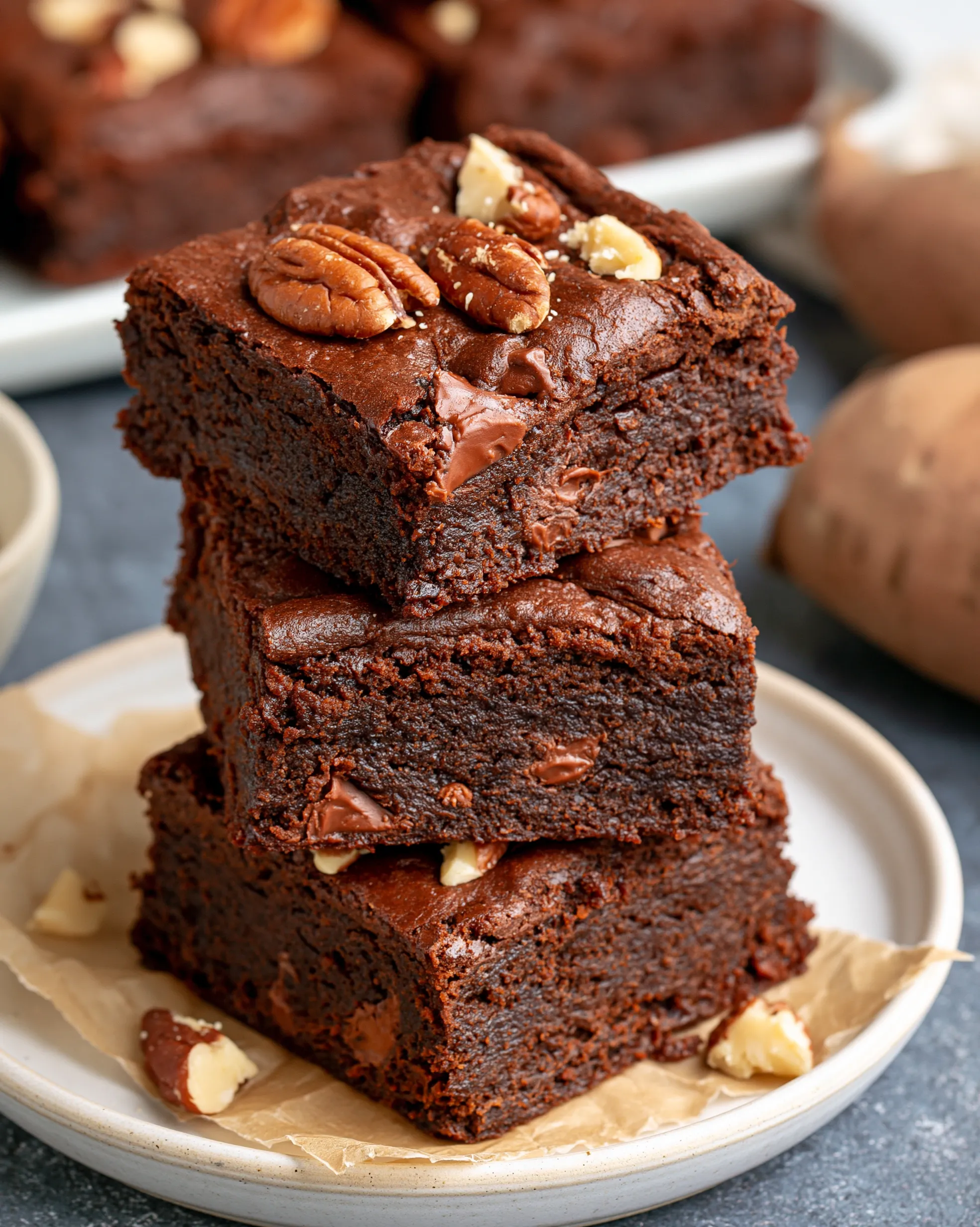 Easy sweet potato brownies recipe — a stack of dark fudgy brownies with melty chocolate chunks, topped with pecan halves and chopped walnuts